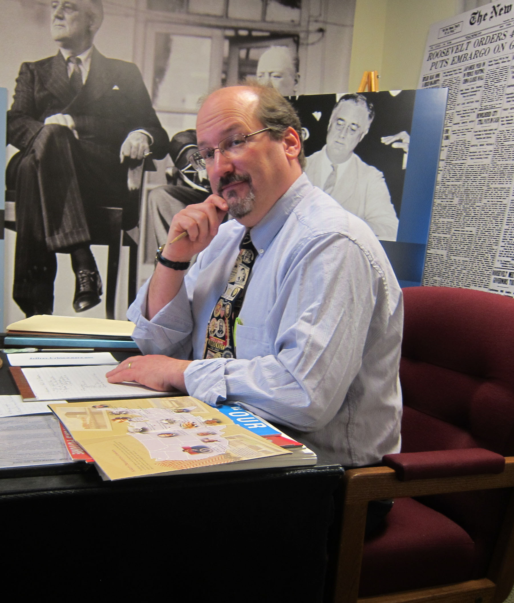 Photo of Jeff Urbin sitting at his desk in a shirt and tie with FDR memorabilia in background